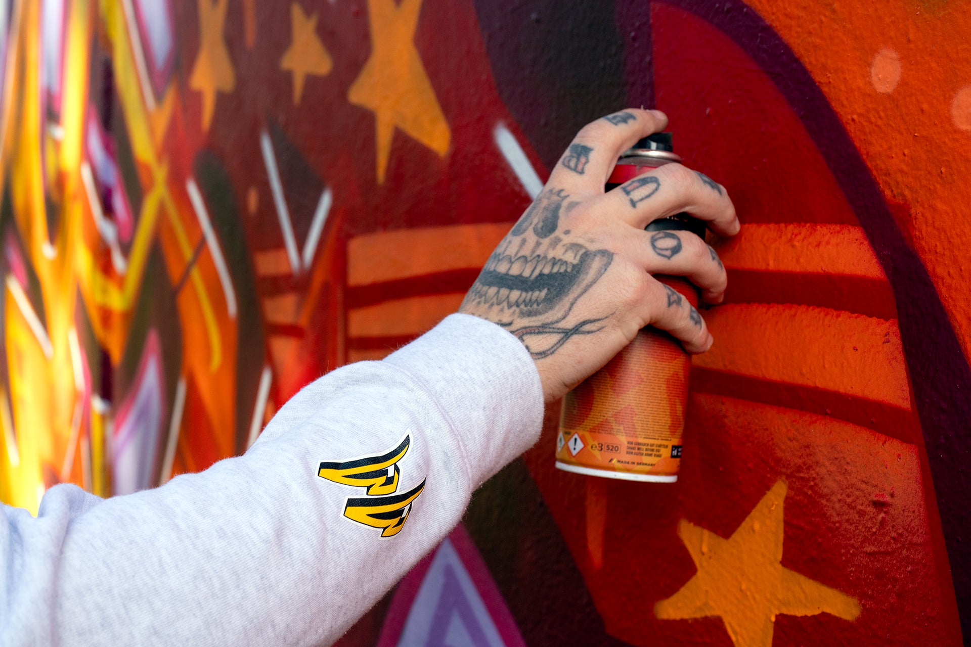 Master Murals' arm wearing a white marle hoodie holding a spray can and graffitiing the wall