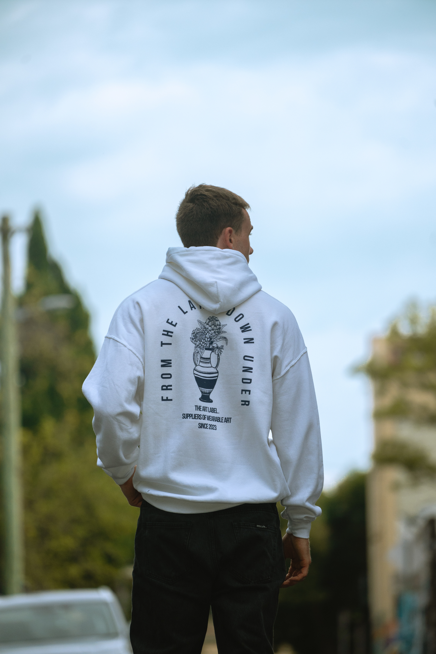 A guy standing on the street facing away from the camera and showing off back piece of wearable art
